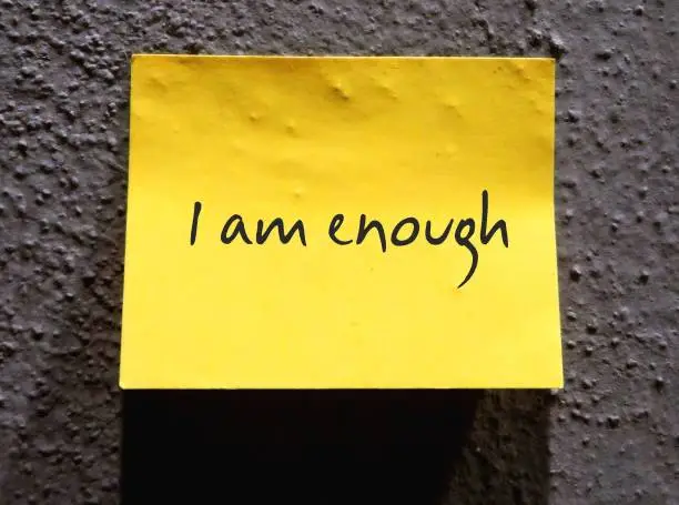 Yellow note paper with handwritten text I AM ENOUGH - concept of positive affirmation, daily self-talk to overcome low self-esteem and build self-acceptance