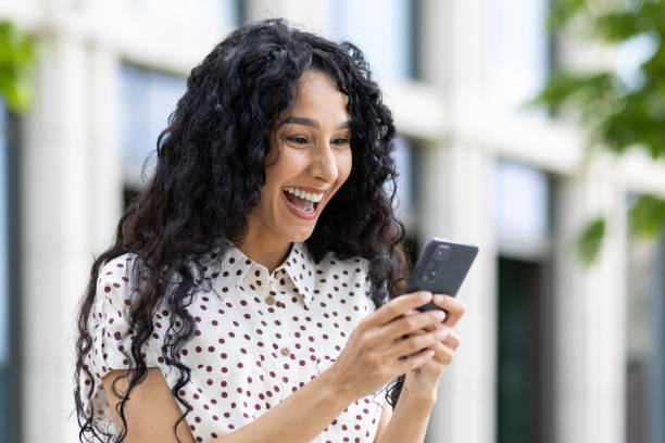 istock Joyful woman with curly hair laughing while looking at smartphone outdoors, modern lifestyle and connectivity 1969349452