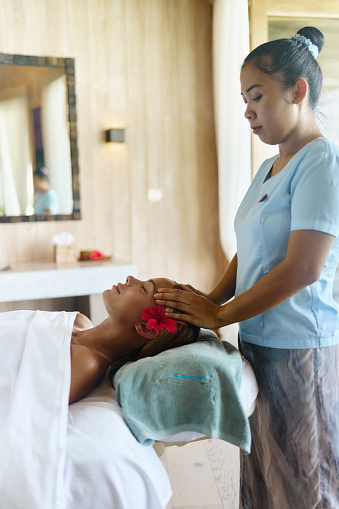 Young woman receiving relaxing head massage from a therapist at the spa.
