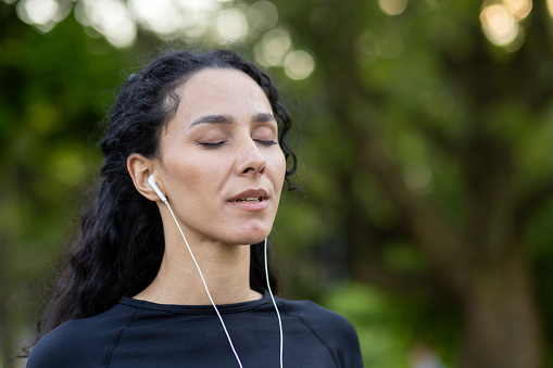 Portrait of a young woman in headphones with eyes closed, walking in the park in the morning, morning yoga, jogging.