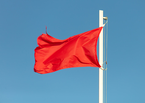 A red high hazard beach caution flag flaps in the wind.