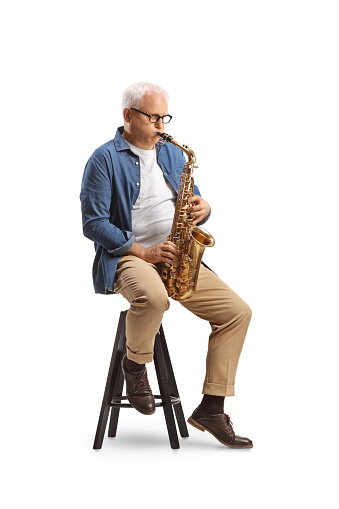 Mature man playing a saxophone and sitting on a chair isolated on white background
