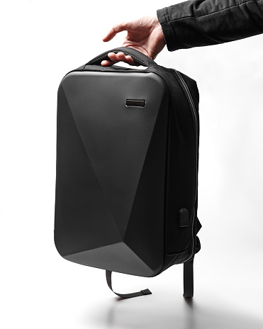 A black modern backpack with an asymmetrical design hangs on the arm on a white background