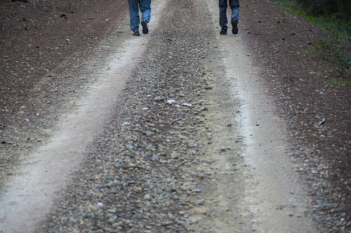 Dirt road shot from top angle. Two people walking see only feet. In motion.