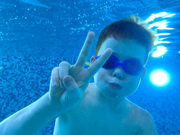 un garçon montrant un signe de paix ou de victoire sous l’eau dans la piscine - mobilestock freedom enjoyment blue photos et images de collection