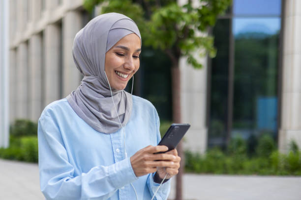 istock Confident muslim woman in hijab using smartphone outside modern office building 1969442419