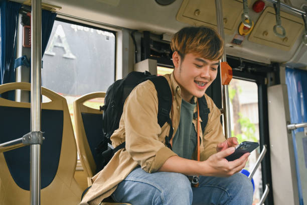 istock Happy young Asian man with backpack commuting by public transport and using mobile phone 1969444055