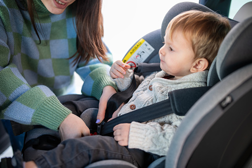 Young mother preparing her son,buckling up his seat belt on the safety seat.