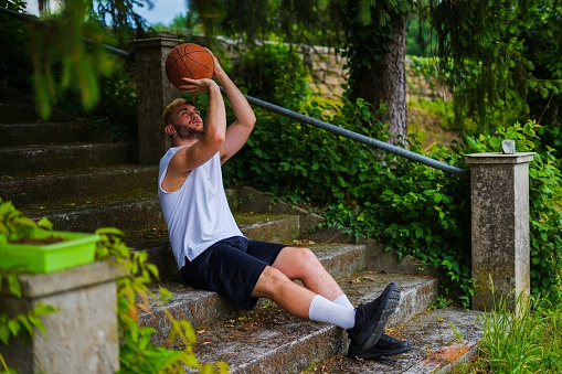 Basketball player throwing a ball like a three point shot while is sitting in a beautiful spot with vegetation