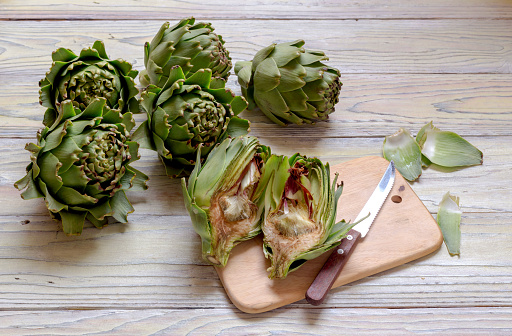 The green, fresh artichokes in the kitchen on a wooden table close-up