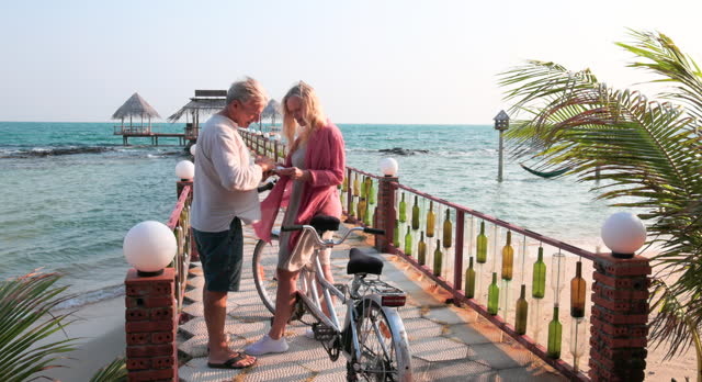 Couple take tandem bicycle to pier, water's edge