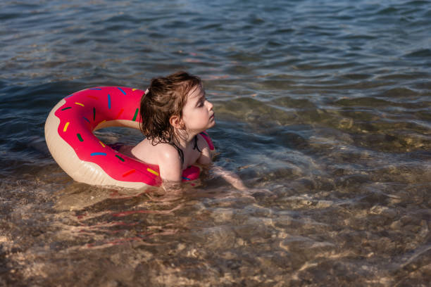 menina bonito no anel de natação inflável nadando no mar durante o dia de verão. - swimming tube inflatable circle - fotografias e filmes do acervo