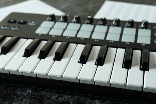 Midi keyboard and music sheets on black smokey table
