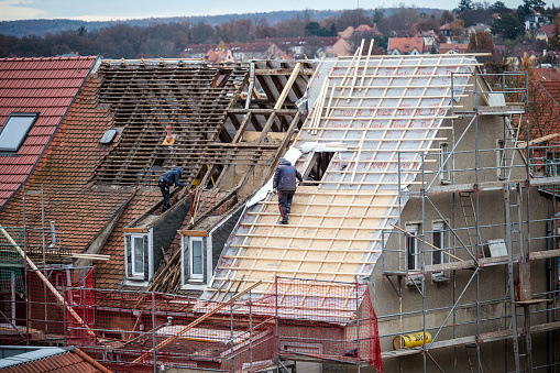 Weimar, Germany - 28. November 2022: Roofers are standing on a roof that is partially covered and the roof truss has already been replaced.