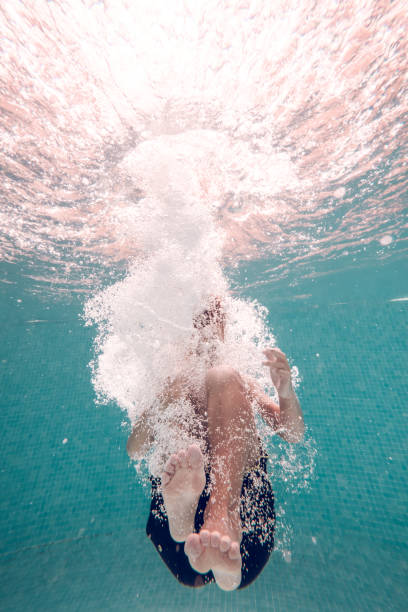 Anonymous boy diving underwater in pool Underwater full body shot of unrecognizable barefoot kid wearing swimming shorts plunging in transparent clean blue water in pool just do it stock pictures, royalty-free photos & images