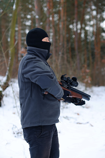A shooting instructor walks through the winter forest with his weapon raised