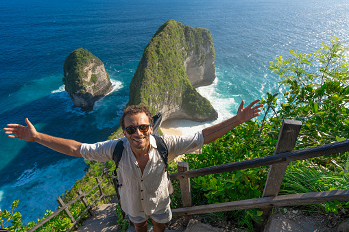 Male tourist visiting Kelingking Beach on the Indonesian island of Nusa Penida. Climbs up the step trail to the top.