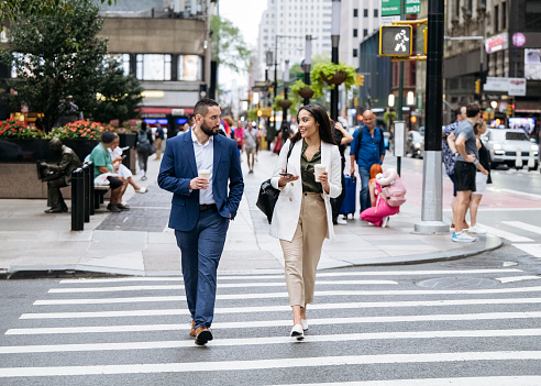 Full length view of male and female associates crossing street side by side, talking and smiling, enjoying break from the office.