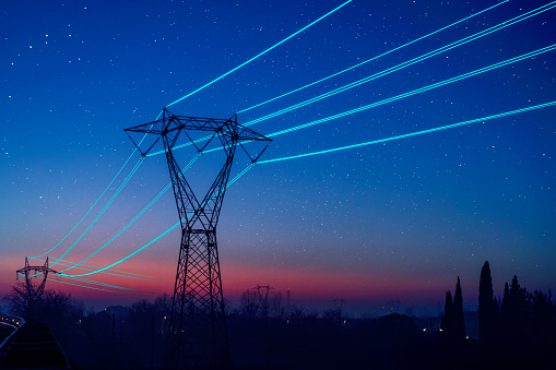Electricity pilon with glowing cables over sunset sky