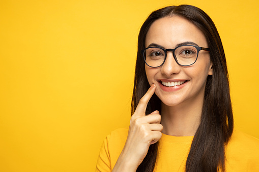 Photo of modern girl gesturing her beaming white heathy teeth with forefingers looking at camera on yellow background