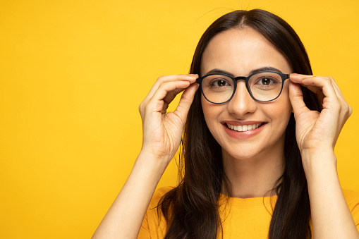 Portrait of lovely positive girl hand touch glasses empty space isolated on yellow color background