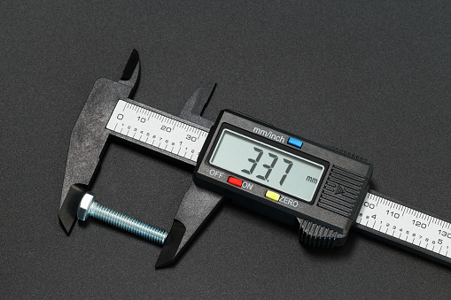 Measuring bolt length using a digital caliper. Macro photography on a dark background