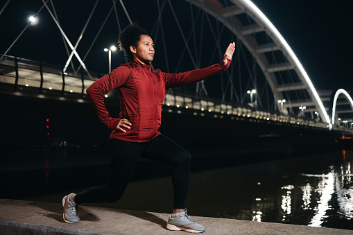 A bridge at night turns into a stage where a mature woman demonstrates her commitment to fitness, stretching in preparation for her exercise routine amidst the urban night