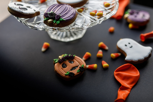 Close up shot of cute Halloween themed cookies served on a cake stand with scattered candy corn against black background.