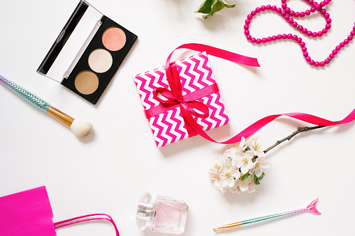 Female workplace of a fashion blogger. Cosmetics, a gift box with a bow. Flat lay on a white background