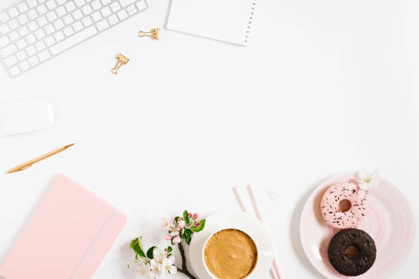 istock Stylish flat lay women's workplace with notebooks, keyboard, pen and spring apple blossoms, a cup of coffee and donuts on a white background with copy space 1969635537