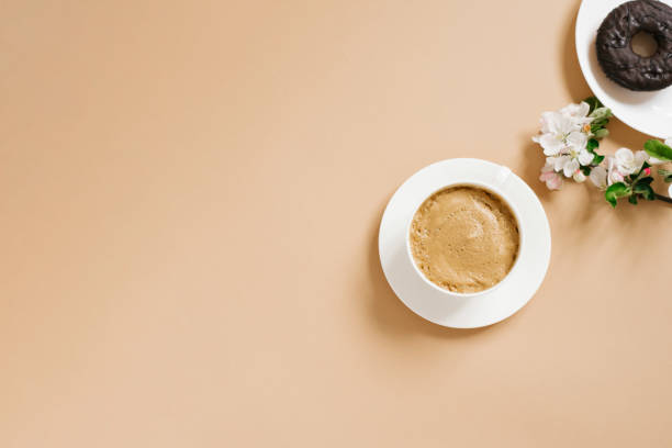 istock Coffee with milk in a white porcelain cup and chocolate donuts with white apple blossoms on a beige background. The concept of a morning breakfast or coffee break 1969641335