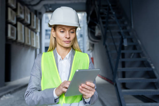 istock Serious confident thinking female engineer with tablet computer inspecting factory wearing hard hat and reflective vest 1969643411