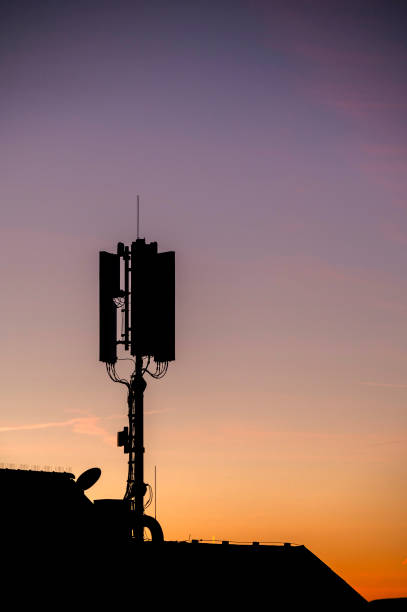 Silhouette of a mobile phone antenna on a roof at dawn.