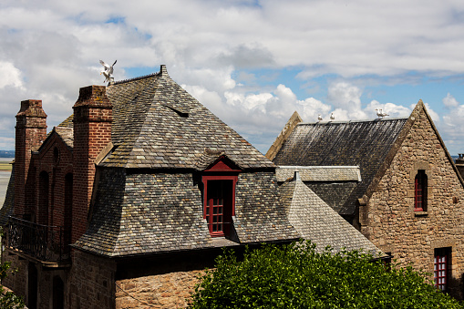 View of the top of a picturesque houses in the Mont Saint Michel with seagulls on roofs at sunny day with lovely sky and clouds. Normandie, Nothern France