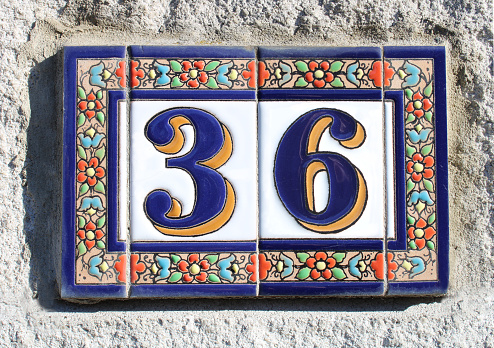 collage from number three and six, house number thirty six, vintage style 3 and 6. ceramic sign made of enamel or clay on a stone wall. a blue and yellow 36 on a  matte, bright,  glossy background. around the two-tone numbers is a blue ceramic frame on which relief-like red and blue flowers with green leaves are drawn. the sun is shining across the numbers. retro numbers for anniversary, birthday vouchers, celebration, coupon card, coupons, voucher present card or invitation
