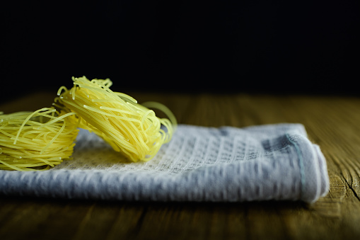 Uncooked pasta nests on towel wooden table on black background