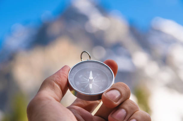 istock Compass in hand. Navigation and travel direction concept. A man with a compass in his hand against the background of high powerful mountains on a sunny day 1969674783