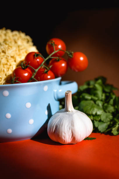 Fresh garlic and cherry tomatoes in bowl with instant noodle on red surface