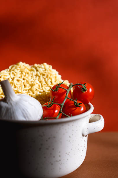 Fresh cherry tomatoes and aromatic garlic with raw instant noodle in bowl on red background