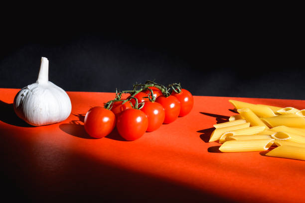 istock Cherry tomatoes and garlic near raw pasta on red surface and black background 1969677531