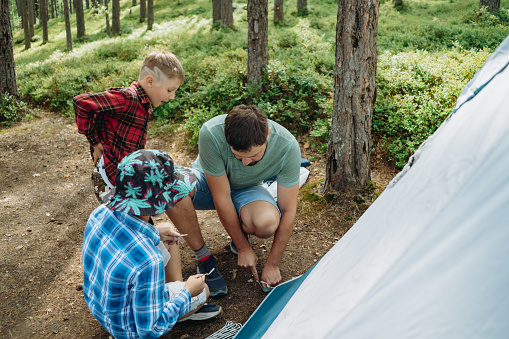 caucasian man putting up a tent in pine forest. children helping him. Family camping concept. High quality photo