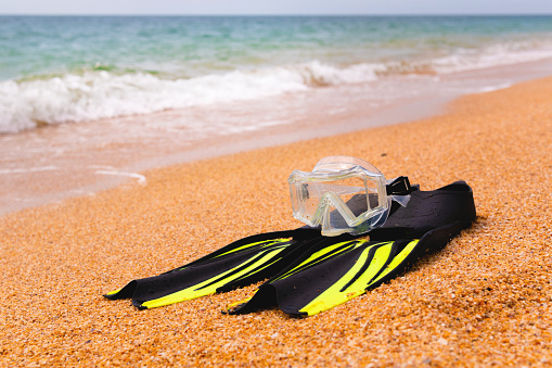A pair of fins and a diving mask on a sandy beach, bottom view. Space for text or advertising of a sports store or beach resort