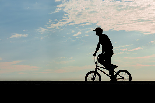 Freestyle cyclist practicing street BMX in backlight at sunset
