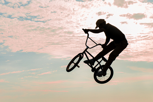 Freestyle cyclist practicing street BMX in backlight at sunset