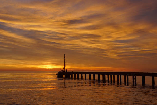 A dramatic sunset sky over the ocean pier in Santa Monica, with birds flying across colorful clouds at the golden hour.