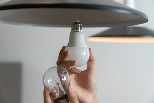 A young woman is changing light bulbs at home, replacing incandescent bulbs with LED bulbs to save electricity