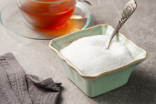 Granulated white sugar in a sugar bowl and a glass cup of tea on the table.