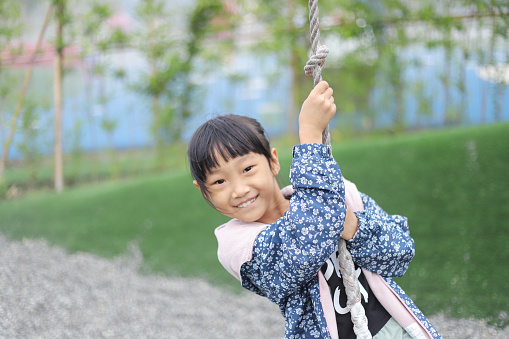 an Asian girl is playing on the single cable pulley in the park. she enjoying the exciting feeling of speed.
