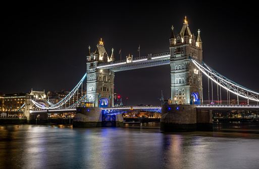 A night time, long exposure view Tower Bridge from The Queens Walk on the south bank of the River Thames showing colourful lights and beautiful light reflections on the water.