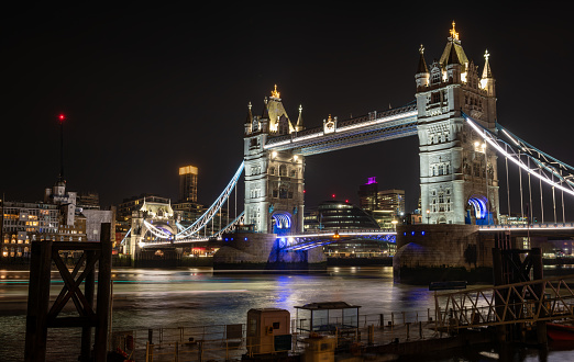 A night time, long exposure view of Tower Bridge from the north side of the Thames river with beautiful light reflections on the water.